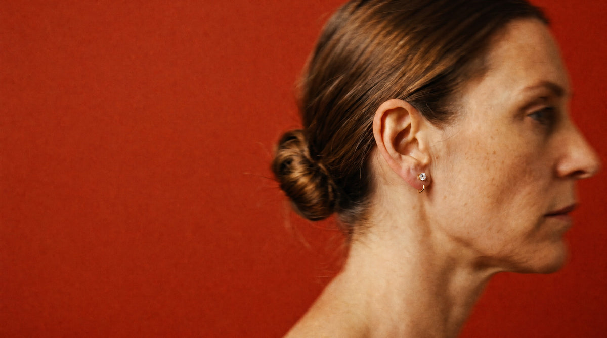 Clear Round Open Hoop worn in the earlobe, in profile against a red wall