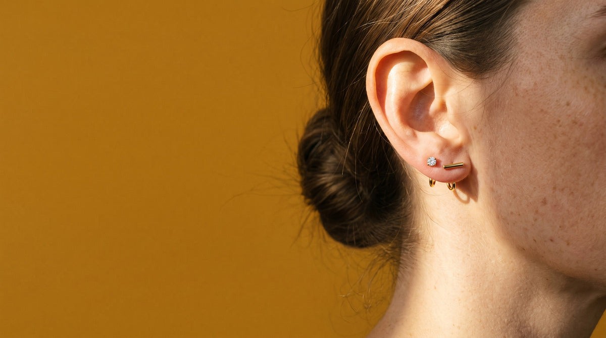 Clear Round Open Hoop and Bar Open Hoop in 18K Gold Vermeil on an ear in profile, against mustard paper in a beam of sun.