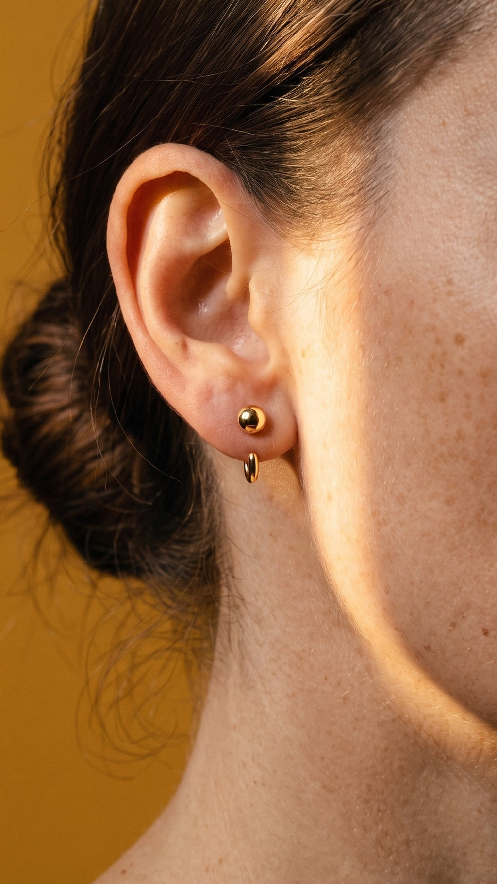 Ball Open Hoop in 18K Gold Vermeil on an earlobe, in a beam of sun on mustard paper.