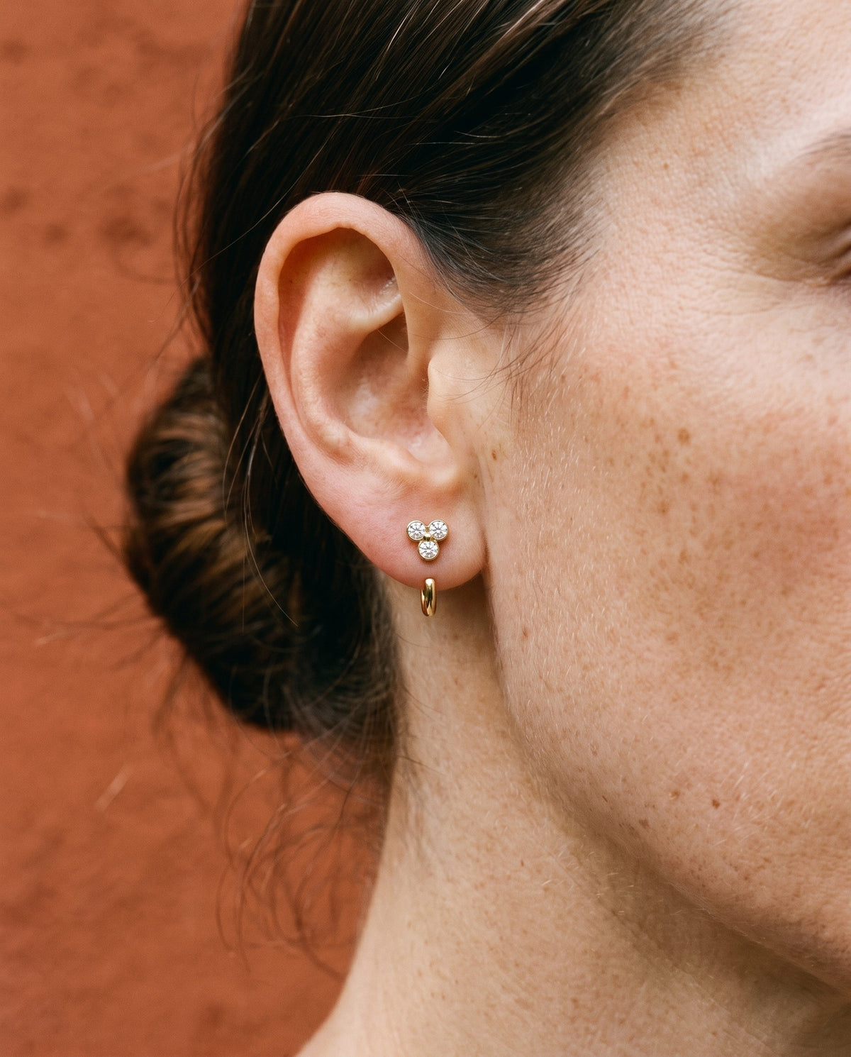 Clear Cluster Open Hoop in 18K Gold Vermeil on an earlobe, against a terracotta wall.