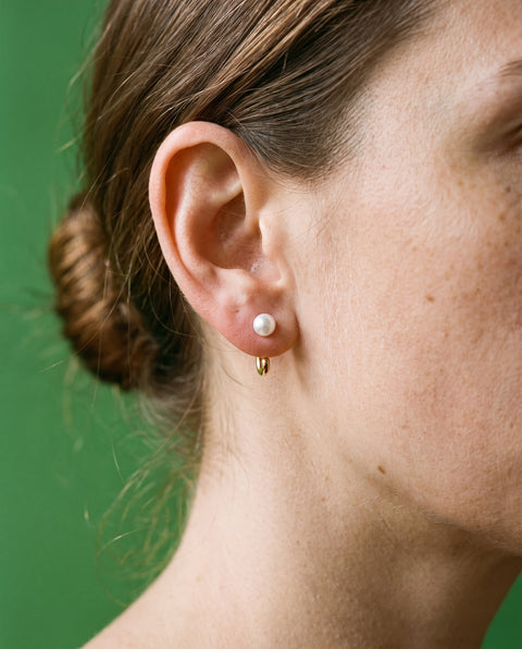 White Bead Open Hoop in 18K Gold Vermeil on an earlobe, against a leaf-green wall.