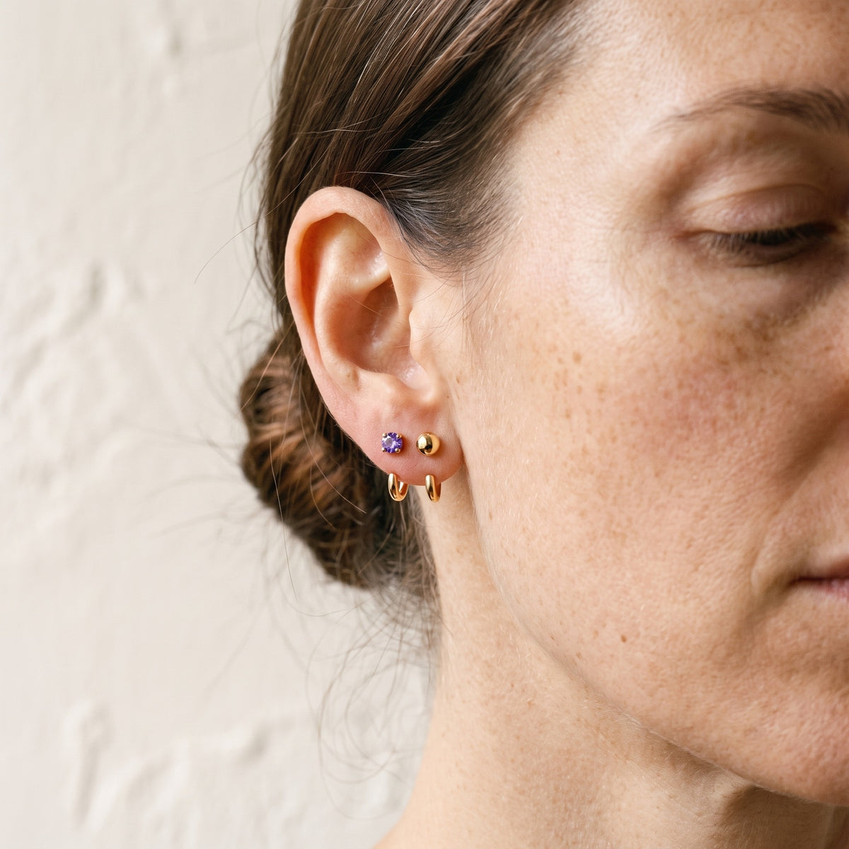 Violet Round Open Hoop and Ball Open Hoop in 18K Gold Vermeil on an ear, against a bone wall.