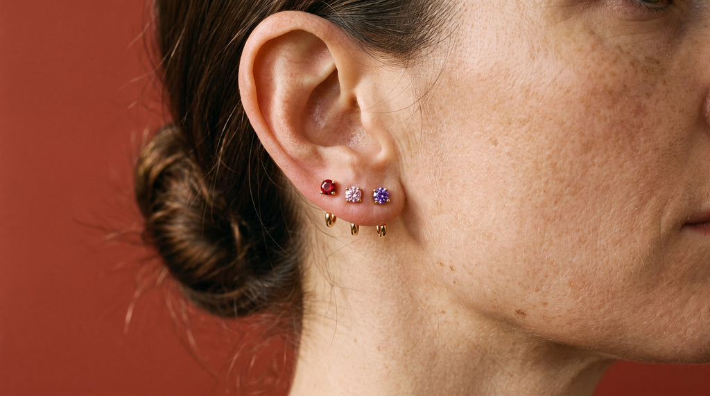 Red, Pink and Violet Round Open Hoops in 18K Gold Vermeil on one ear, against brick-red paper.