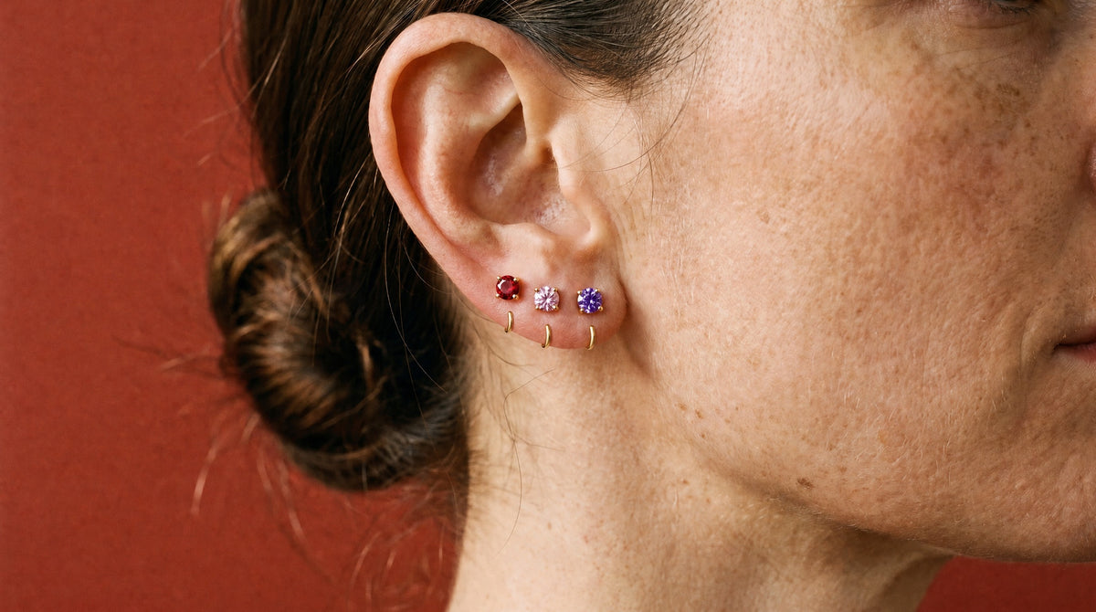 Red, Pink and Violet Round Open Hoops in 18K Gold Vermeil on one ear, against brick-red paper.