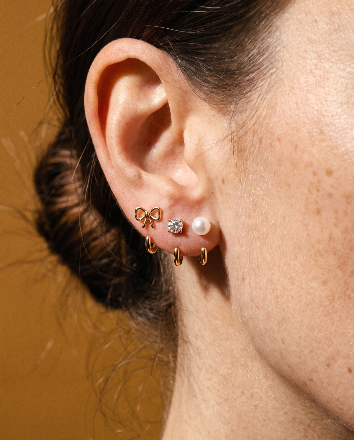 The Bow, Clear Round and White Bead set in 18K Gold Vermeil on one ear, against mustard paper.