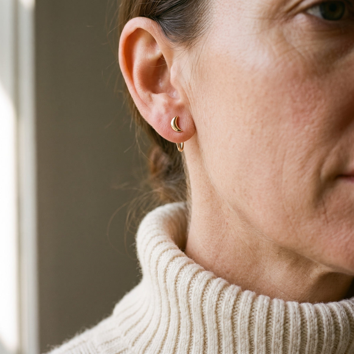 Crescent Open Hoop in 18K Gold Vermeil on an earlobe, above a cream knit collar.