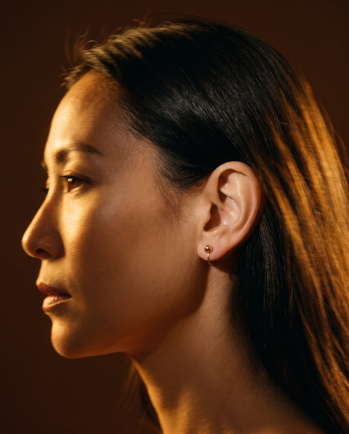 Clear Cluster Open Hoop in 18K Gold Vermeil on an ear in profile, in warm light against a dark wall.