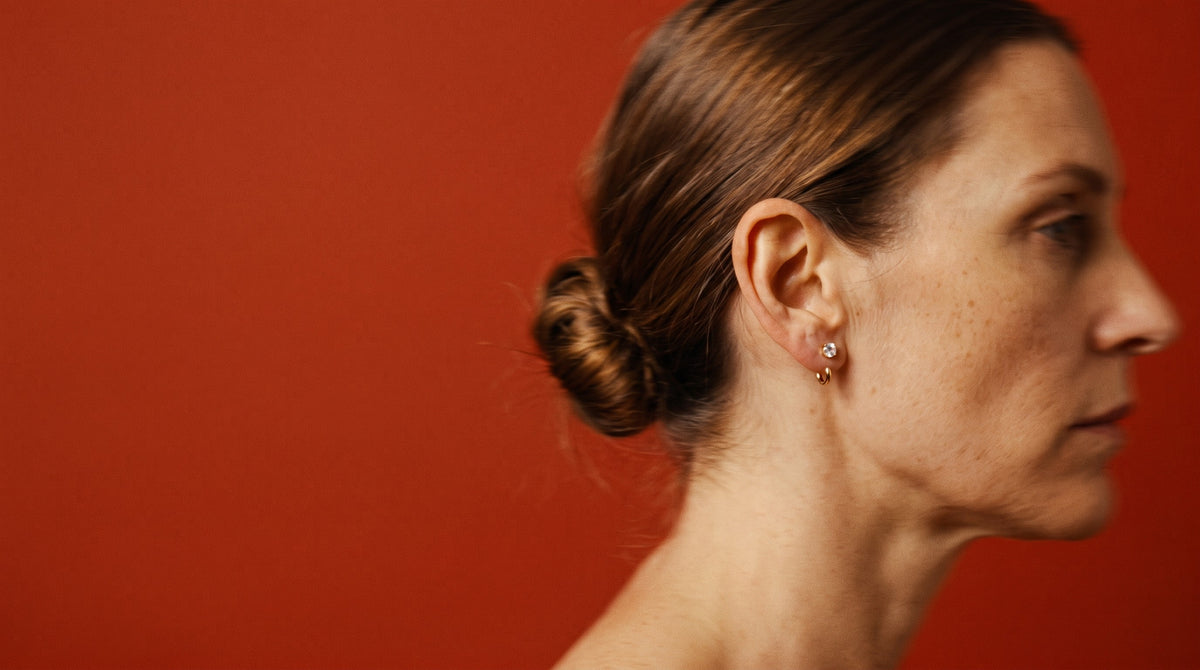 Clear Round Open Hoop worn in the earlobe, in profile against a red wall