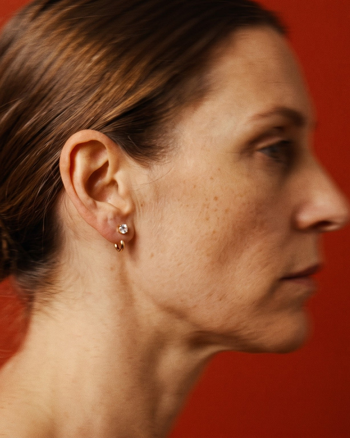 Clear Round Open Hoop worn in the earlobe, in profile against a red wall