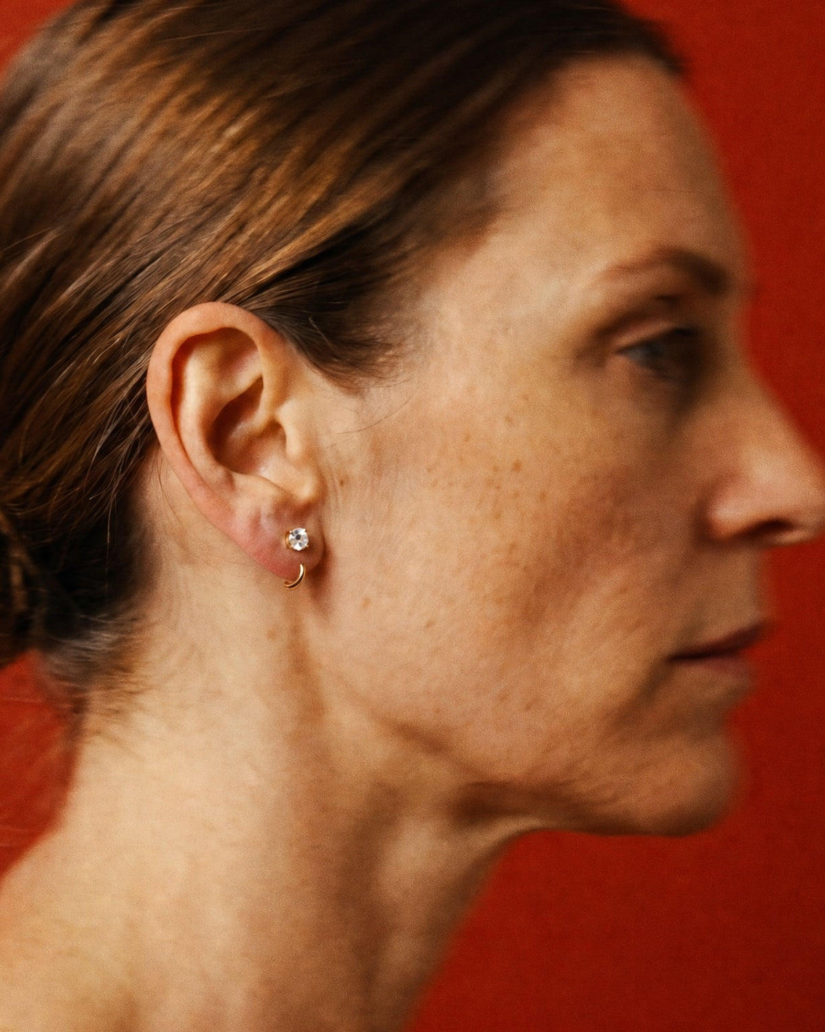 Clear Round Open Hoop worn in the earlobe, in profile against a red wall