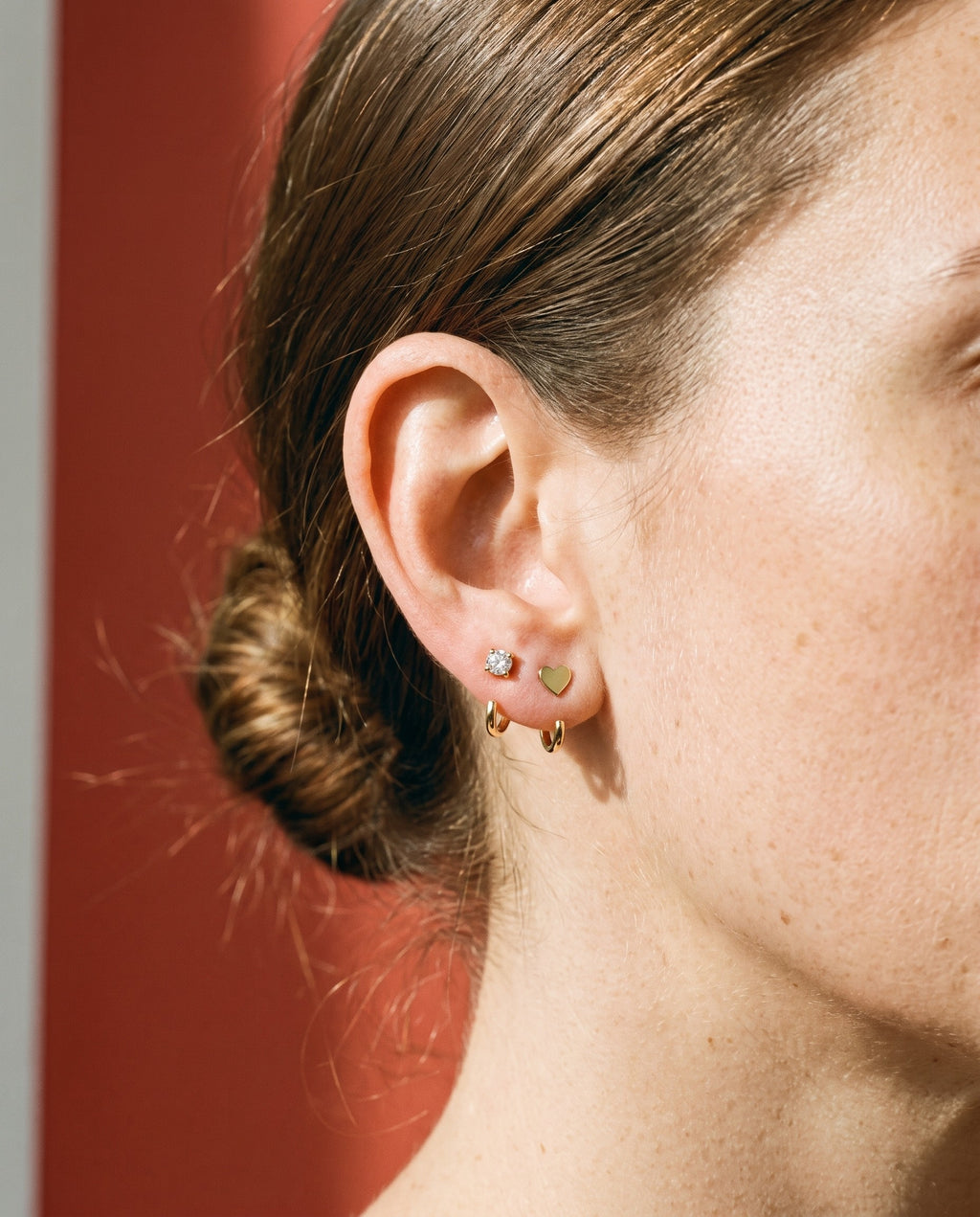 Clear Round Open Hoop and Heart Open Hoop in 18K Gold Vermeil on an ear, against brick-red paper.