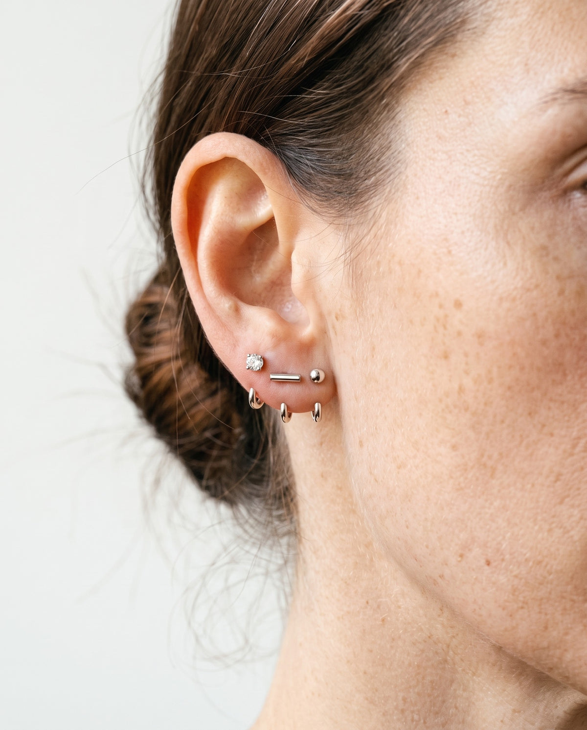 The Clear Round, Bar and Ball set in Sterling Silver on one ear, in window light against a bone wall.