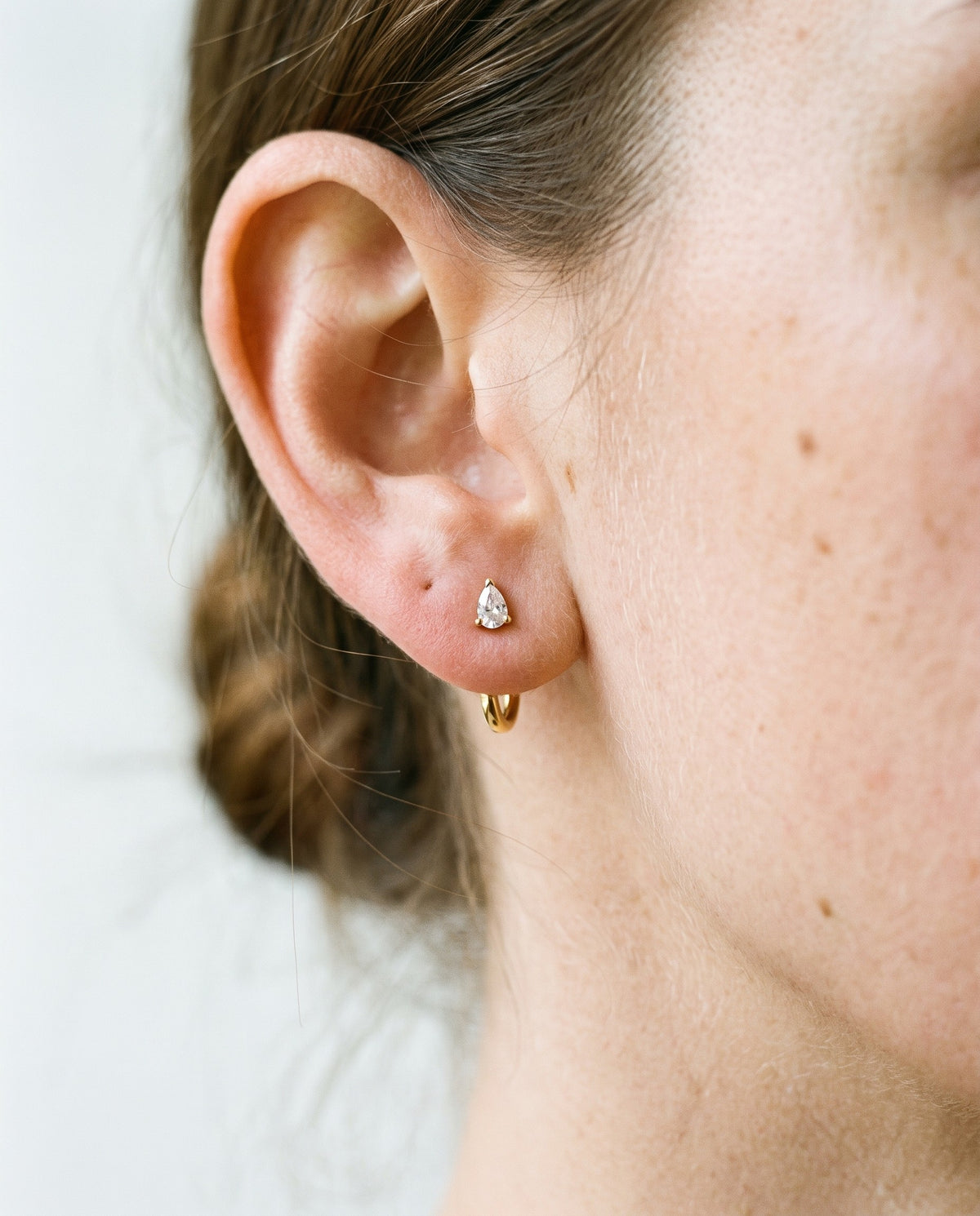 Clear Teardrop Open Hoop in 18K Gold Vermeil on an earlobe, against a bone wall.