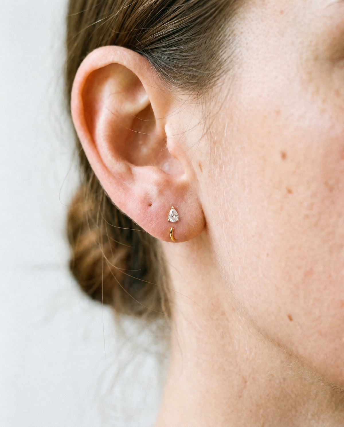 Clear Teardrop Open Hoop in 18K Gold Vermeil on an earlobe, against a bone wall.
