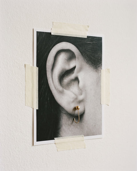 Ball Open Hoop in 18K Gold Vermeil pinned through a printed photograph of an ear, taped to a white wall.