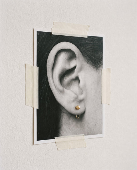 Ball Open Hoop in 18K Gold Vermeil pinned through a printed photograph of an ear, taped to a white wall.